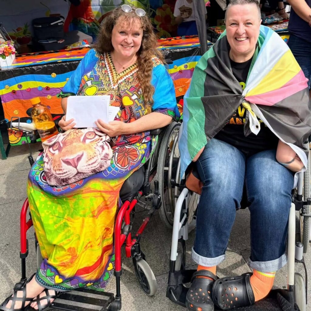 Patricia Koller (links: im bunten Kaftan) und Jacqueline Ernst. Beide sitzen lachend im Rollstuhl